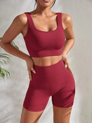 Model wearing Zen Yoga Shorts Set in red. Soft textured rib knit tank top with matching slim fit high waist shorts provide support and comfort during your movements. Model stands with hands on her hips in front of a white background.