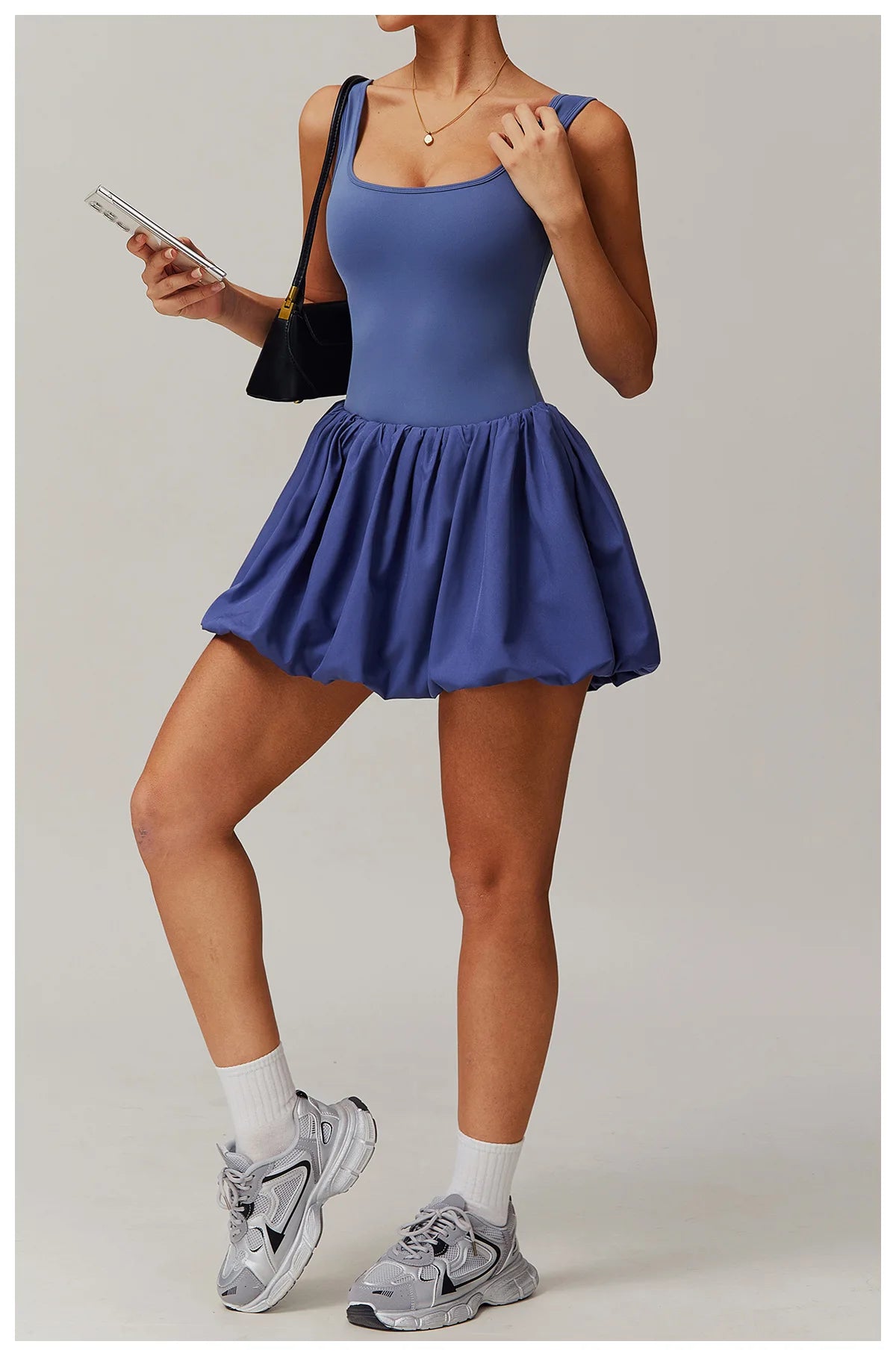 Full length front view of a model wearing the peri purple Rinay Sport Dress from ShoptheKei activewear collection. Sleeveless tank dress with gathered skirt at waist seam and blouson hem. Stretchy and cute dress design for sports and casual strolls. Paired with crew socks and gray sneakers.