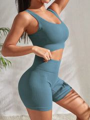 Model wearing Zen Yoga Shorts Set in cactus green. Soft textured rib knit tank top with matching slim fit high waist shorts provide support and comfort during your movements. Model stands to the side with a hand on her waist and the other rests at her head in front of a white background.