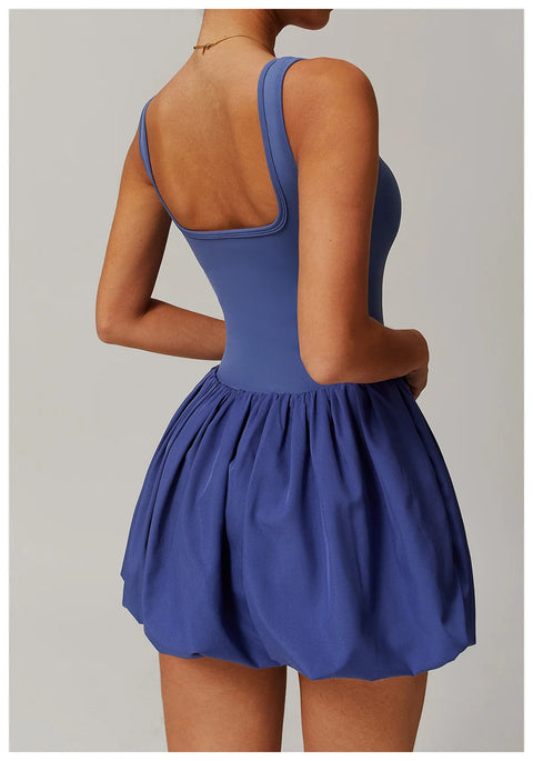 Back view of a model wearing the peri purple Rinay Sport Dress from ShoptheKei activewear collection. Sleeveless tank dress with a low square shaped back neckline, gathered skirt at waist seam, and blouson hem. Stretchy and cute dress design for sports and casual strolls.