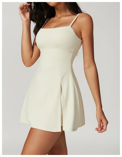 Close up view of the Bree Yoga Dress in creme color. Features thin spaghetti straps, straight neckline, fitted bodice, and A-line skirt with a pronounced side slit. Mini-length dress photographed against a neutral background.