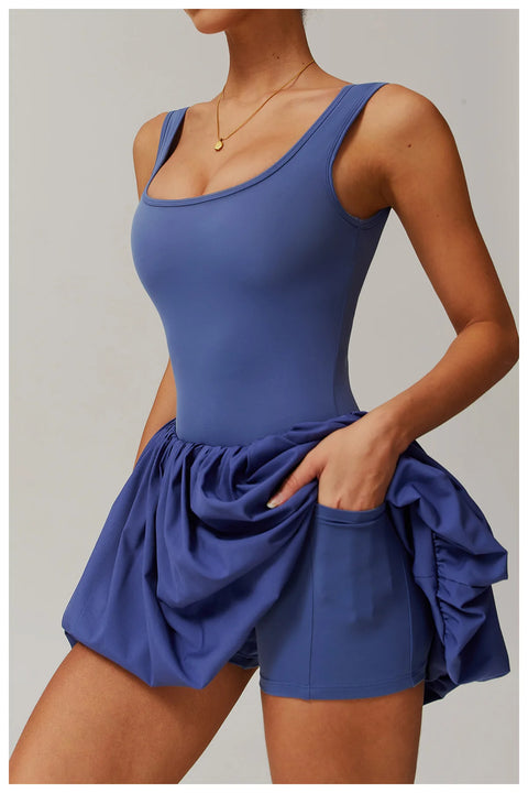 Side view of a model wearing the peri purple Rinay Sport Dress from ShoptheKei activewear collection. Image reveals a pair of shorts sewn inside the dress and flat side pocket large enough for a phone or gym card.