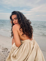 Isla Summer Dress from Shop the Kei -Close up back view showcases natural linen dress soft textile texture and elegant drape. Romantic dress is worn by a model with soft brunette waves sitting on the beach