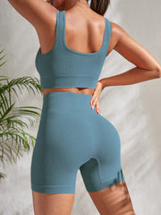 Back view of model wearing Zen Yoga Shorts Set in cactus green. Soft textured rib knit tank top with matching slim fit high waist shorts provide support and comfort during your movements. Model stands strong with a hand on her waist as the other rests at her head in front of a white background.