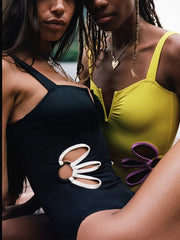 Model wearing Gabby One Piece Swimsuit in black from ShoptheKei.com. Retro-inspired tank top with split neckline, side flower cut outs, and white trim. Close up shows smooth fabrication surface