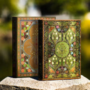 Two ornate books with intricate designs on a stone surface with a blurred natural background