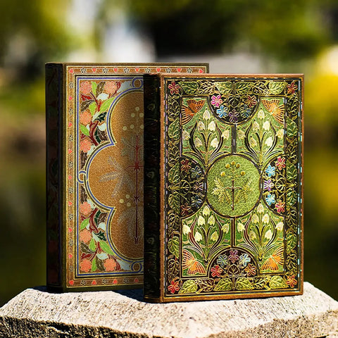 Two ornate books with intricate designs on a stone surface with a blurred natural background