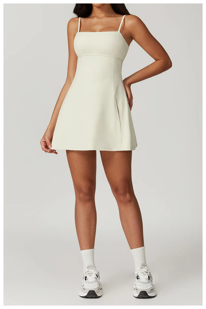 Front view of the Bree Yoga Dress in creme color. A mini dress with thin spaghetti straps, straight neckline, fitted bodice, and short A-line skirt. Model poses with white ankle socks and chunky athletic sneakers against a neutral background.