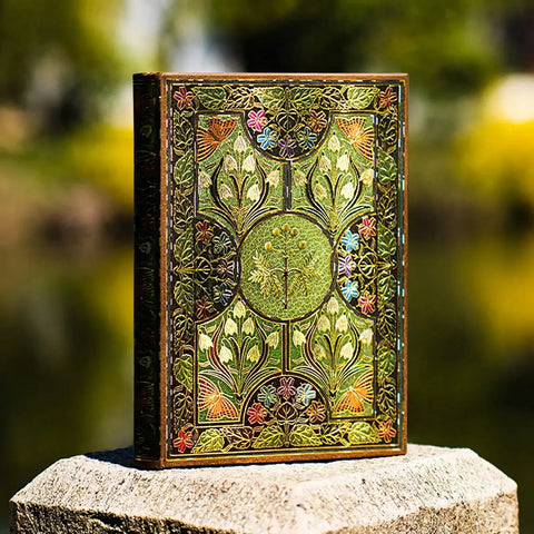 Decorative book with intricate floral patterns on a stone surface with a blurred natural background