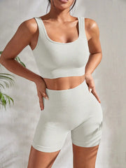 Model wearing Zen Yoga Shorts Set in white. Soft textured rib knit tank top with matching slim fit high waist shorts provide support and comfort during your movements. Model stands with hands on her hips in front of a white background.