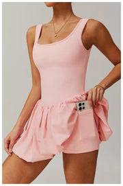 Side view of a model wearing the pink Rinay Sport Dress from ShoptheKei activewear collection. Image reveals a pair of shorts sewn inside the dress and flat side pocket large enough for a phone or gym card.