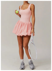 Full length front view of a model wearing the pink Rinay Sport Dress from ShoptheKei activewear collection. Sleeveless tank dress with gathered skirt at waist seam and blouson hem. Stretchy and cute dress design for sports and casual strolls. Paired with crew socks and gray sneakers.