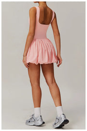 Full length back view of a model wearing the pink Rinay Sport Dress from ShoptheKei activewear collection. Sleeveless tank dress with gathered skirt at waist seam and blouson hem. Stretchy and cute dress design for sports and casual strolls. Paired with crew socks and gray sneakers.