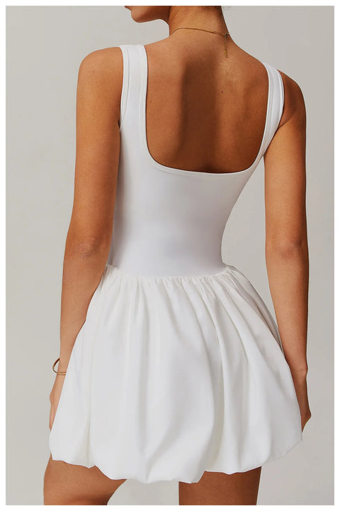 Back view of a model wearing the white Rinay Sport Dress from ShoptheKei activewear collection. Sleeveless tank dress with low square shaped back neckline, gathered skirt at waist seam, and blouson hem. Stretchy and cute dress design for sports and casual strolls.