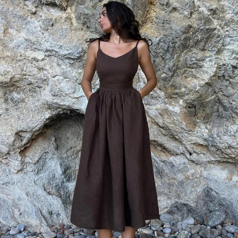 Isla Summer Dress from Shop the Kei -Brunette model wearing a coconut brown linen dress with gathered waist and v neckline and spaghetti straps. Dress fits at the bust and flares at the waist gathers. Photographed against a natural stone background.