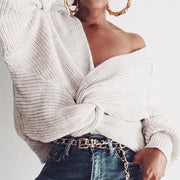 Close-up view of the Aries Sweater in milk white featuring a distinctive twisted front knot design. The chunky knit sweater is styled with blue jeans, worn off-shoulder with a wrap-style closure that creates a cropped silhouette. Product photography against a white background showcasing the sweater's chunky rib knit texture, soft yarns, relaxed fit, and versatile styling.