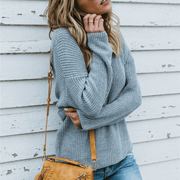 Close up front view of a model wearing gray colored Aries Sweater from Shop The Kei. The chunky knit sweater is styled with light blue jeans and a tan purse. Showcasing the sweater's chunky knit texture, soft relaxed fit, and versatile styling.