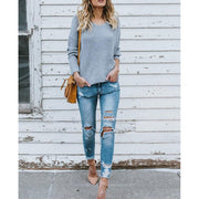 Full length front view of a model wearing gray colored Aries Sweater from Shop The Kei. The v neck chunky knit sweater is styled with distressed jeans, strappy heels, and a tan purse. Showcasing the sweater's soft, casual style and relaxed fit