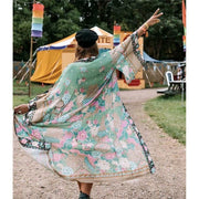 Music festival goer holds up a peace sign wearing Nyma Kimono from Shop The Kei swim coverup collection with black boots and hat. Bohemian-style Nyma Kimono with floats open revealing airy open shape, wing sleeves, and light floral print rayon fabric. Elegant and flowy jacket style