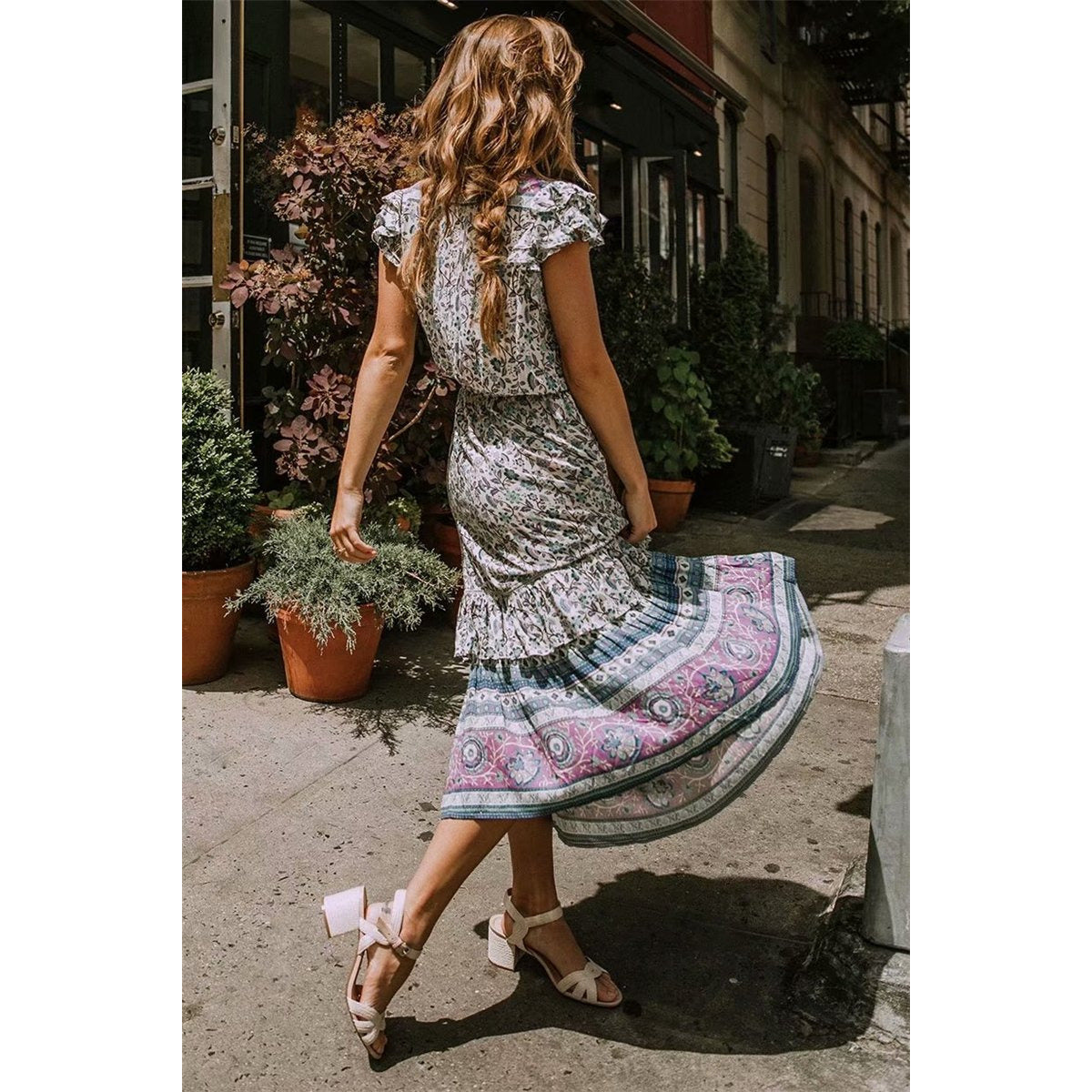 Nala Midi Dress from Shop The Kei - Back view of blue and purple floral boho midi dress with flounce hem and ruffle sleeves, worn by a brunette woman twirling in nude heels