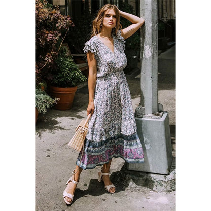 Nala Midi Dress from Shop The Kei - Blue and purple floral boho midi dress with flounce hem and ruffle sleeves, worn by a brunette woman standing at a street lamp post, paired with strappy nude heels and a straw purse